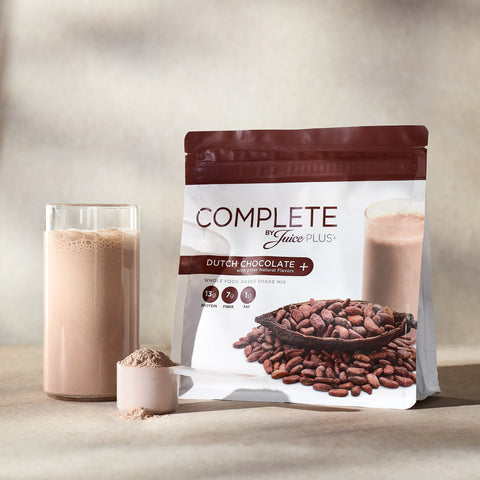 Complete by Juice Plus+ Dutch Chocolate supplement package with a glass of chocolate milk and scoop of powder.