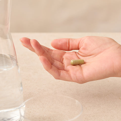 Hand holding a Juice Plus+ supplement capsules with a glass of water on a neutral background