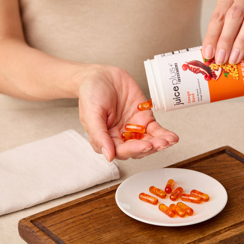 Person holding a Juice Plus+ omega package with orange capsules on a wooden surface