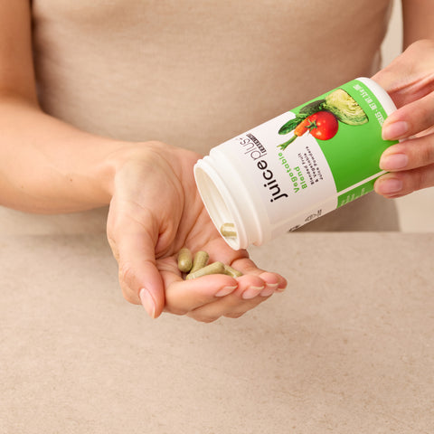 Person holding a bottle of Juice Plus+ Vegetable supplements with capsules in their hand on a beige background