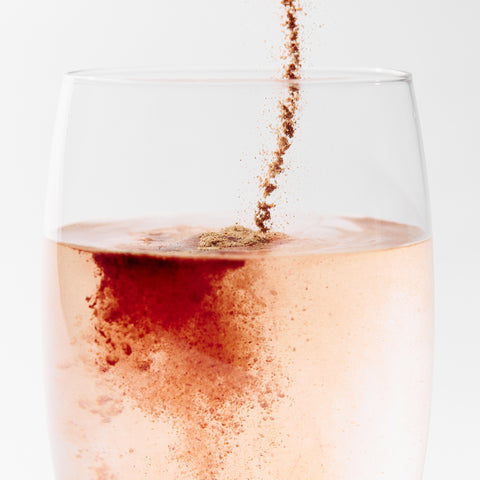 Glass of water being mixed with Juice Plus+ Luminate on a white background