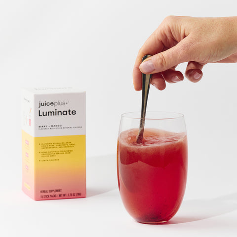 Juice Plus+ Luminate package and a person stirring it in a glass.