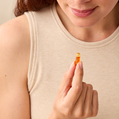 Woman holding a Juice Plus+ Omega supplement capsule close to her face