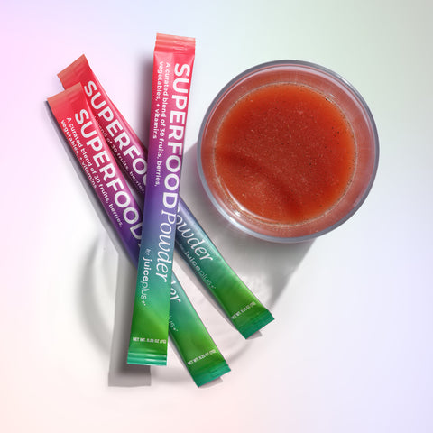 Juice Plus+ Superfood powder packets with a bowl of red juice on a white background