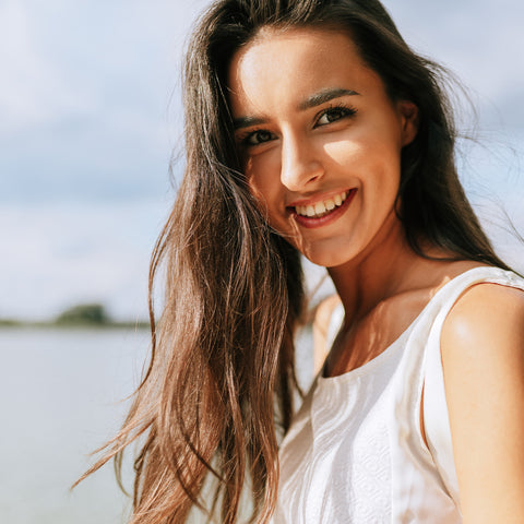 Woman with long brown hair smiling outdoors with a blurred natural background
