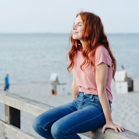Woman with red hair sitting on a wooden bench by the sea