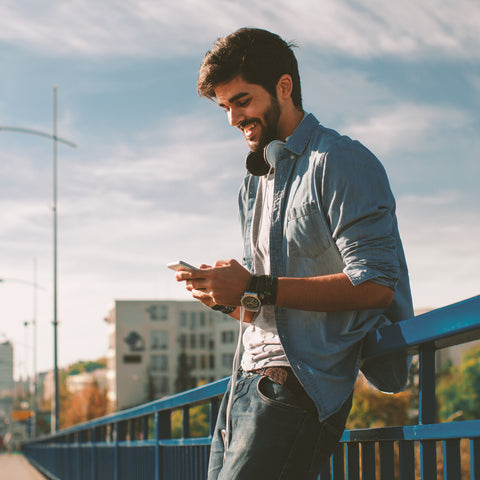 Man using a smartphone on a bridge with a cityscape background