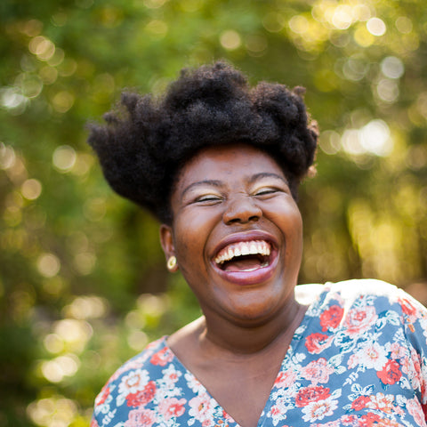 Woman laughing outdoors with a blurred green background