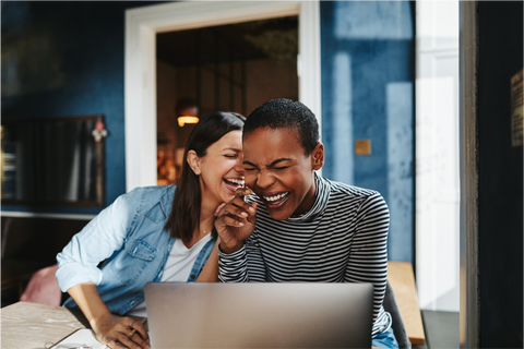 Two women sitting around table laughing with one of them with a laptop in front of her