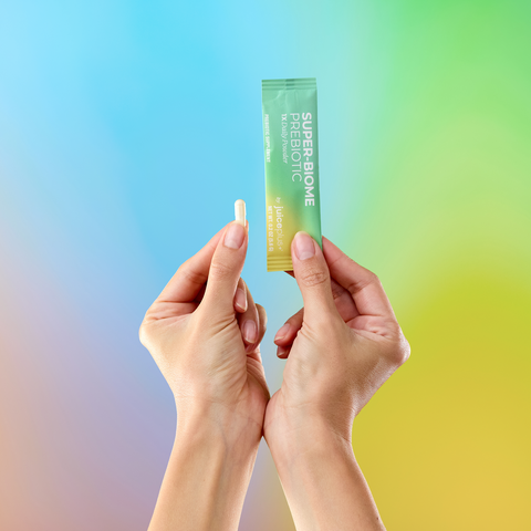 Two hands holding a green packet labeled Juice Plus+ Super-Biome against a gradient background