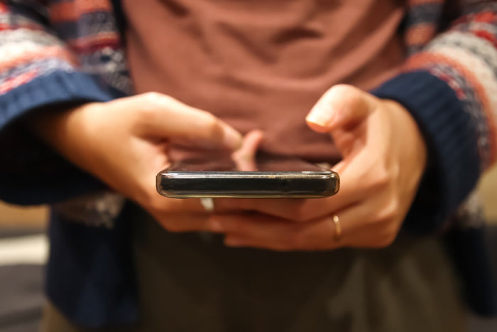A close-up image of someone holding a phone with their hands, with both hands hovering over the screen showing they are engaged with it. 