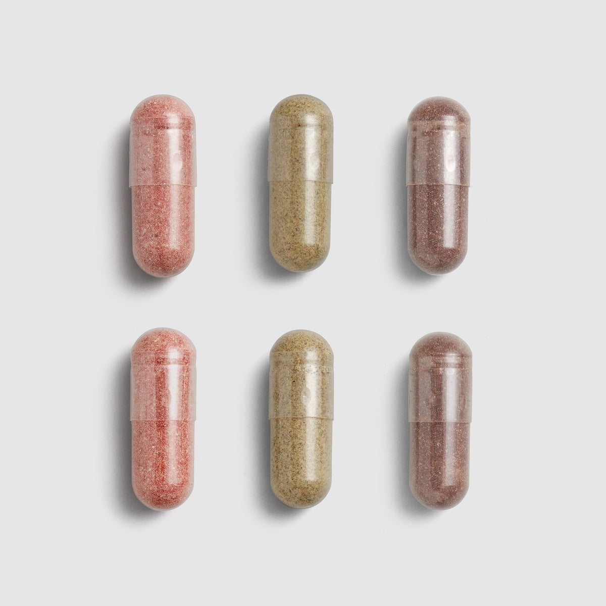 Six Juice Plus+ capsules, three pink and three beige, arranged in two rows on a light gray background.