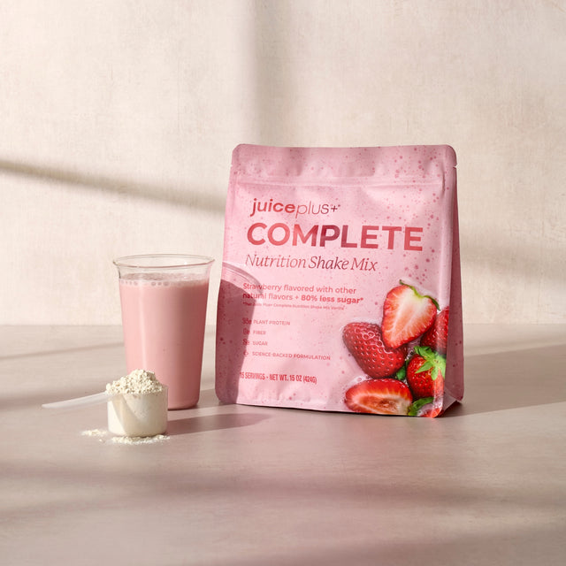 Juice Plus+ Complete Nutrition Shake Mix package with a glass of pink shake and scoop on a light background