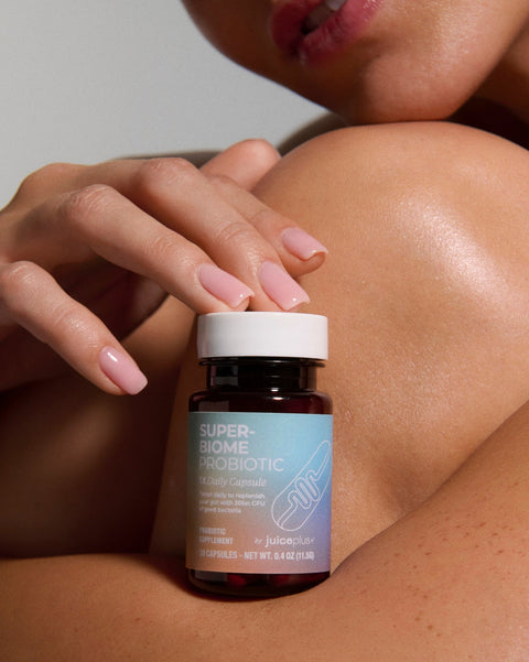 Person holding a bottle of Super-Biome Probiotic by Juice plus+ on a neutral background