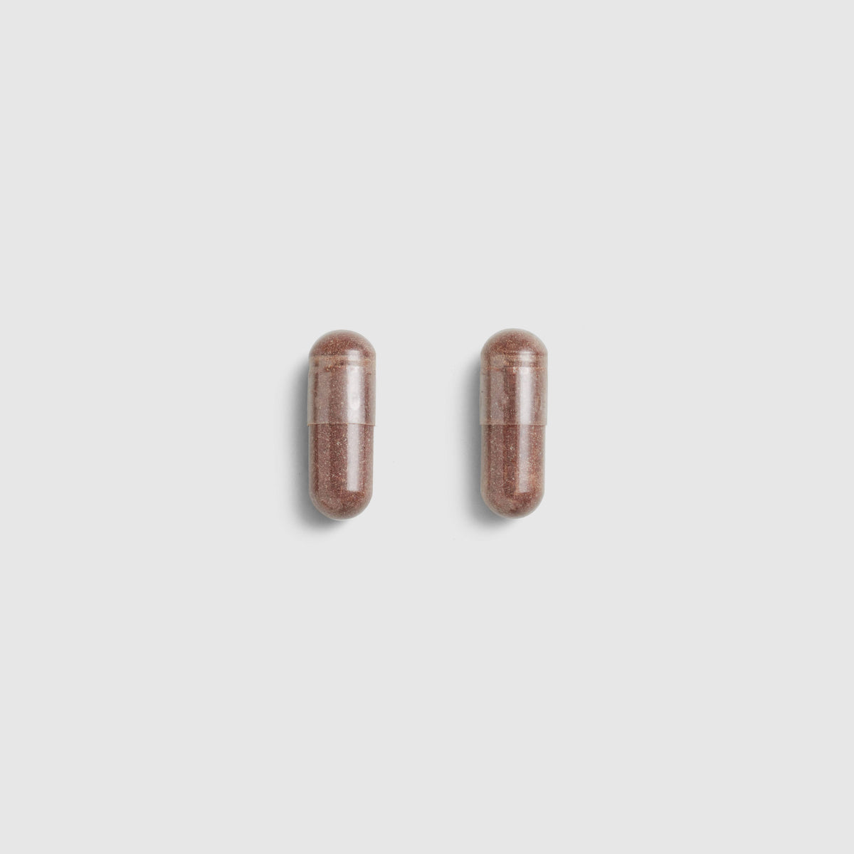 Two brown Juice Plus+ Capsules on a light gray background