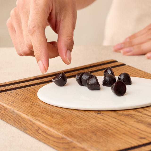 Hand arranging Juice Plus+ Chewables on a white plate with a wooden cutting board.