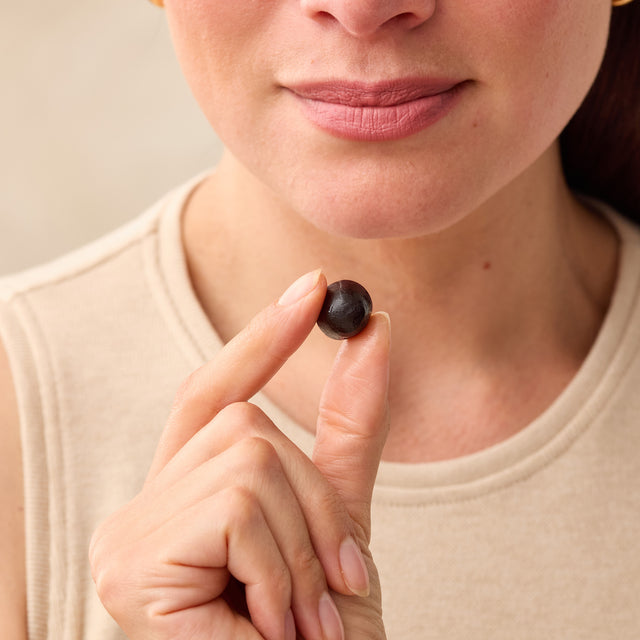Person holding a Juice Plus+ berry Chewable between their fingers against a neutral background