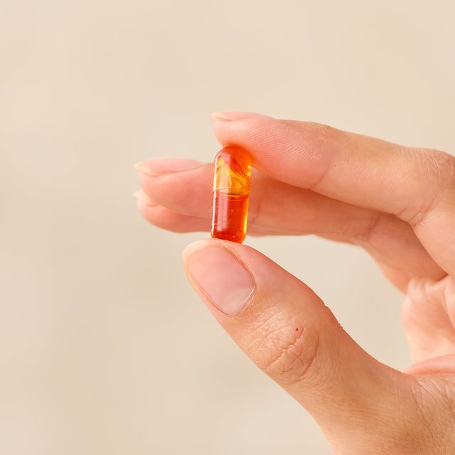 Hand holding a multicolored Juice Plus+ capsule against a beige background