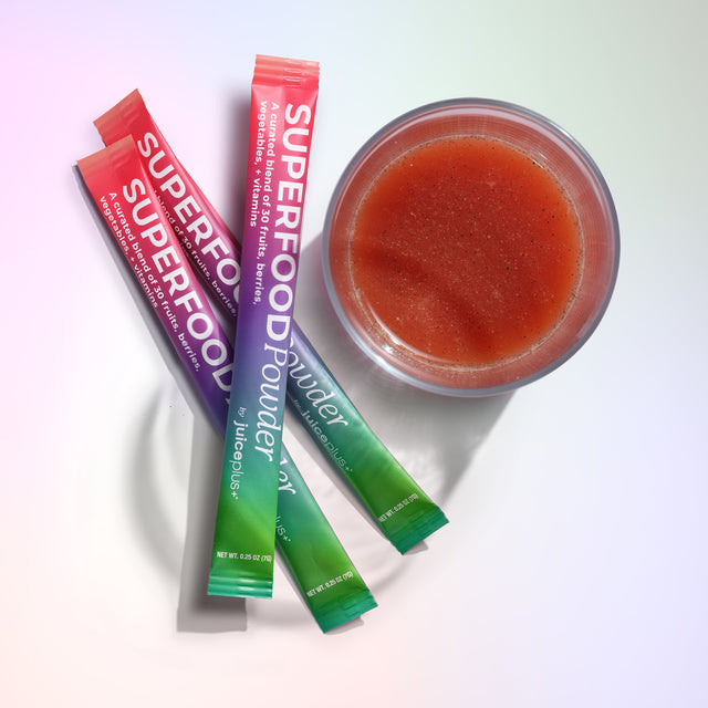 Juice Plus+ Superfood powder packets with a bowl of red juice on a white background