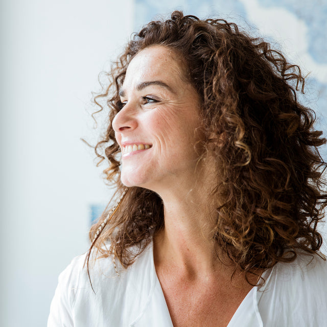 Woman with curly hair wearing a white shirt against a light background