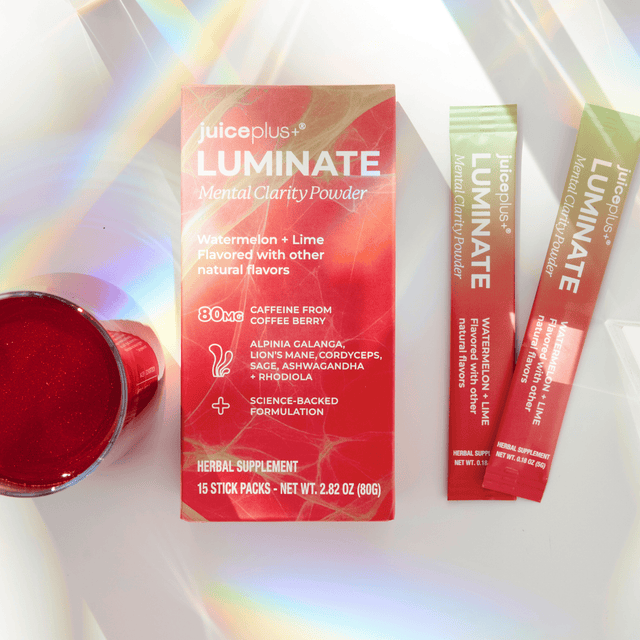 Juiceplus+ LUMINATE Mental Clarity Powder herbal supplement packaging, including a red box, two single-serve packets, and a small red cup on a white surface with a rainbow light effect.