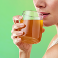 Person holding a glass mug of tea against a green background