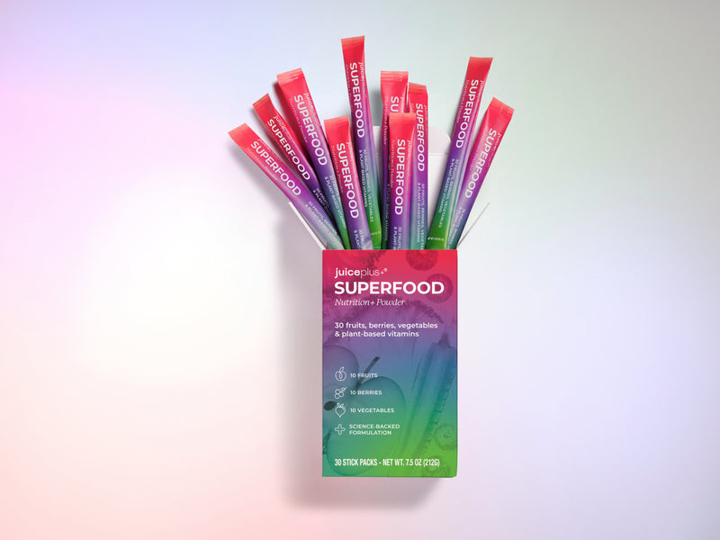 A box of Nature's One Superfood Nutrition+ Powder with multiple colorful stick packs fanned out above it on a soft pastel gradient background.