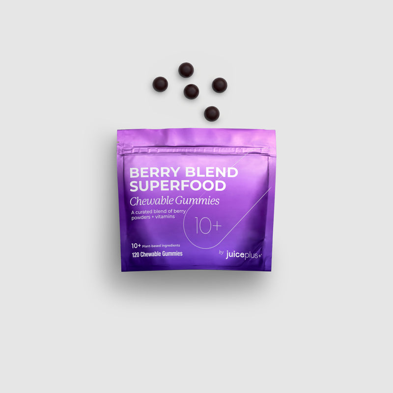 A purple stand-up pouch labeled 'Berry Blend Superfood Chewable Gummies' with five dark round gummies placed above it on a light gray background.