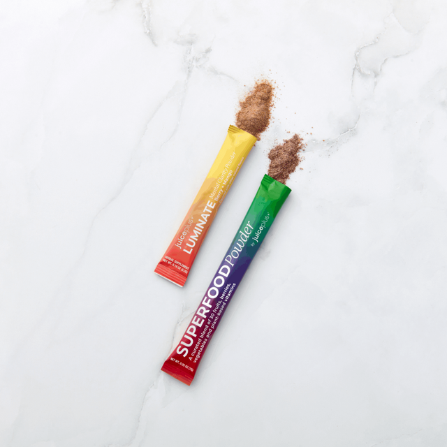 Two colorful superfood and Luminate powders on a light marble surface
