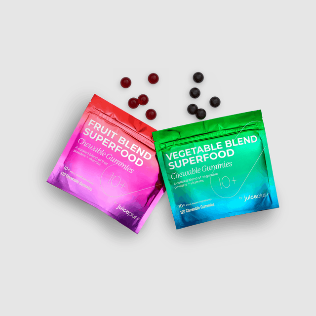 Two packets of juiceplus+ gummies, one pink and one green, with scattered gummies on a light gray background.